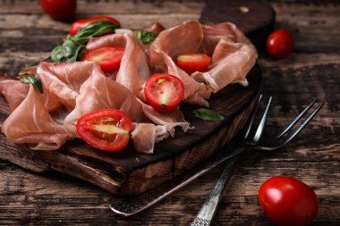 Fesleğenli domates ahşap kesme tahtası, antika arka plan üzerinde ince dilim jambon ile karışık
