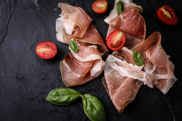 Thin slices of prosciutto with mixed with basil, cherry tomatoes on wooden cutting board,vintage background — Stock Photo, Image