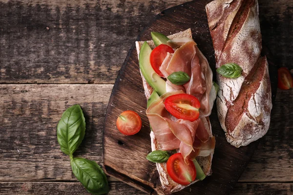 Ciabatta sandwich with prosciutto,avocado,cherry tomatoes and basil on dark background — Stock Photo, Image