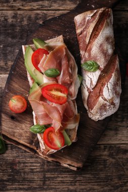 Ciabatta sandviç salam, avokado, kiraz domates ve fesleğen koyu arka plan üzerinde