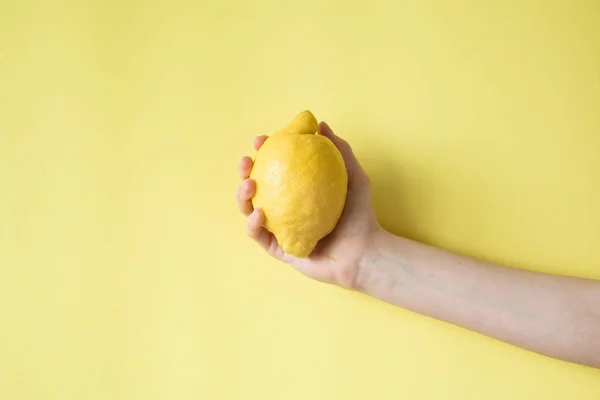 Lămâie în mâna femeii pe un fundal galben — Fotografie, imagine de stoc