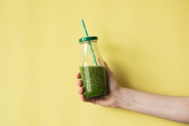 Smoothie shake renkli duvara tutan kadın el. İçme yeşil sağlıklı güler yüzlü kavramı.