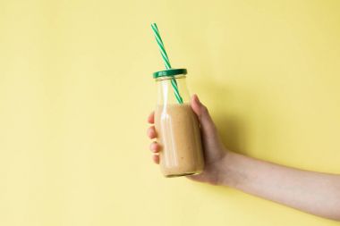 Smoothie shake renkli duvara tutan kadın el. İçme sarı sağlıklı güler yüzlü kavramı.