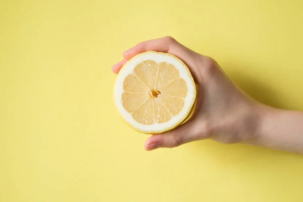黄色の背景に女性の手にレモン — ストック写真