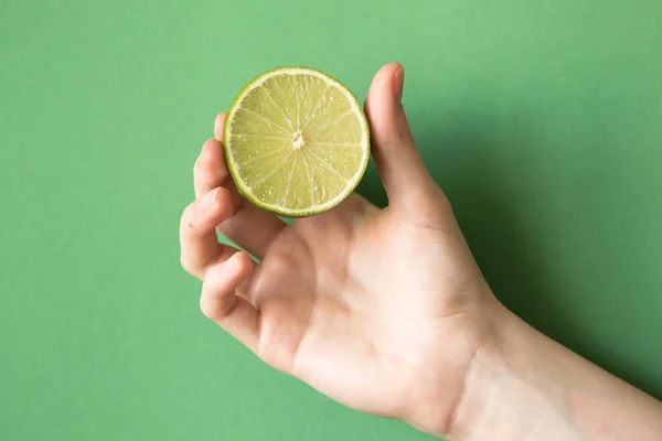 Limão verde saboroso suculento fresco em uma mão humana no fundo verde — Fotografia de Stock