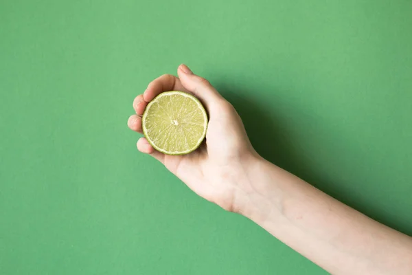Limão verde saboroso suculento fresco em uma mão humana no fundo verde — Fotografia de Stock