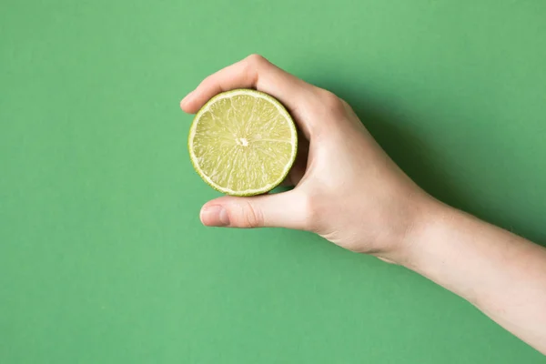 Limão verde saboroso suculento fresco em uma mão humana no fundo verde — Fotografia de Stock