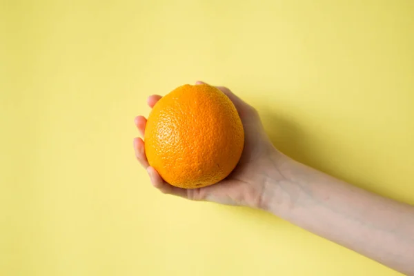 背景が黄色の食品のコンセプトにオレンジを持っている手 — ストック写真