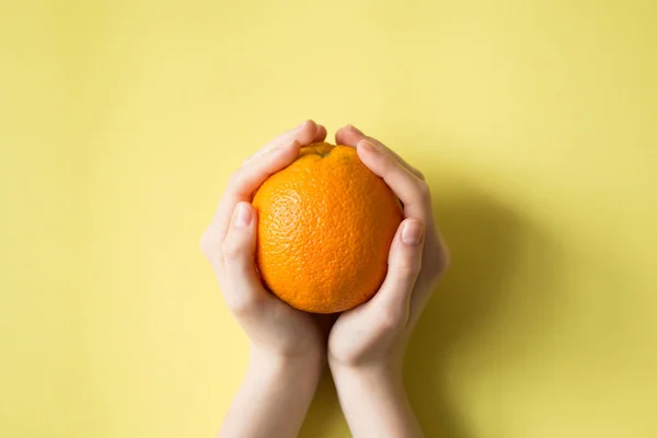 Mão segurando laranja no conceito de comida de fundo amarelo — Fotografia de Stock