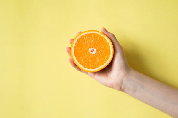 Hand holding orange on yellow background food concept