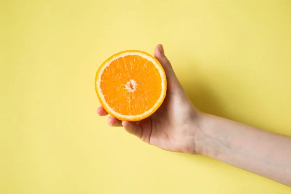 Ręka trzyma orange na żółtym tle jedzenie koncepcja — Zdjęcie stockowe