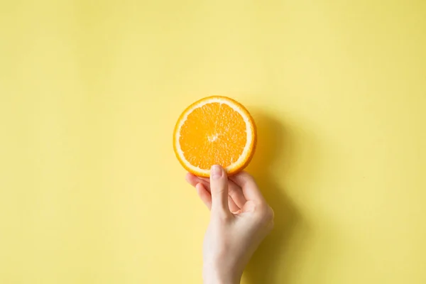 Mão segurando laranja no conceito de comida de fundo amarelo — Fotografia de Stock