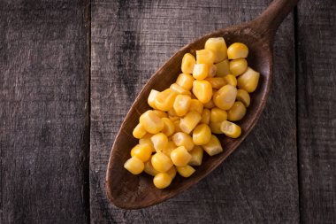 Ahşap masa üzerinde bir kapta tatlı mısır taneleri. Pişmiş konserve sarı sebze, vejetaryen besini.