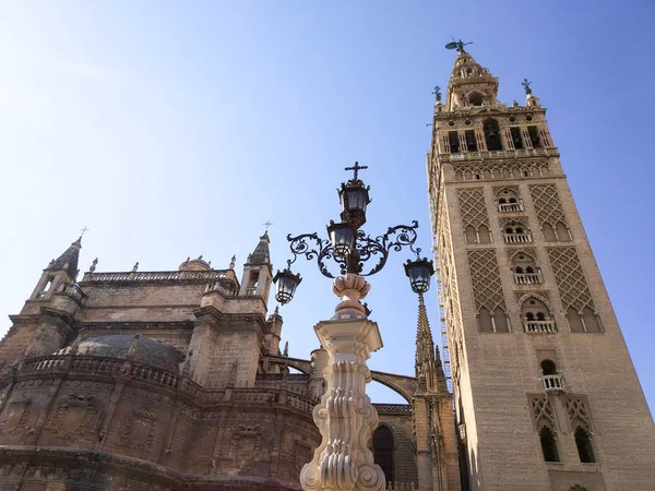 Vista de la Giralda de Sevilla y de la Catedral de Sevilla junto a una farola de luz, Fotografia realizada en dia despejado sin nubes y cielo azul - Fotografia realizada el 31 de Octubre del 2017, Sevilla, Andalucia, Espana, Europa
