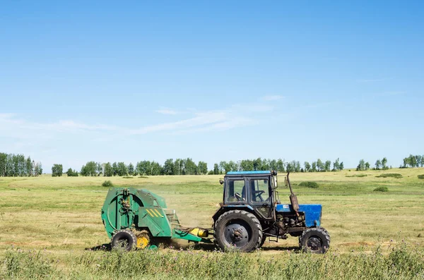 Трактор с прицепным укладчиком, снимает с поля сено — стоковое фото