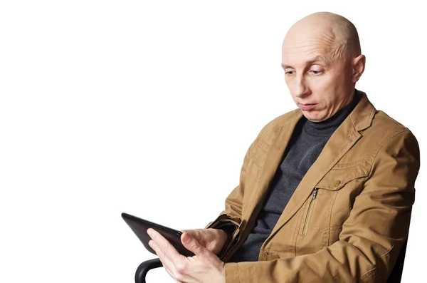 Человек в жёлтой куртке смотрит на планшетный компьютер, сидящий в офисном кресле — стоковое фото