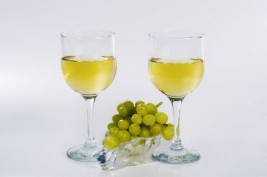 İki kadeh beyaz şarap ve bir demet bir cam tabakta Yeşil üzüm