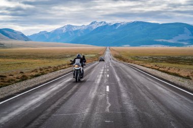 Bir motosikletçi elini kaldırarak selamlıyor, şafak vakti Chuysky otoyolu boyunca gidiyor, bir otobanı olan manzara. Rusya, Altai Dağı