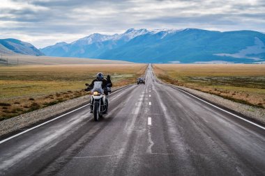 Bir motosikletçi elini kaldırarak selamlıyor, şafak vakti Chuysky otoyolu boyunca gidiyor, bir otobanı olan manzara. Rusya, Altai Dağı