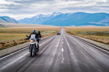 Bir motosikletçi elini kaldırarak selamlıyor, şafak vakti Chuysky otoyolu boyunca gidiyor, bir otobanı olan manzara. Rusya, Altai Dağı