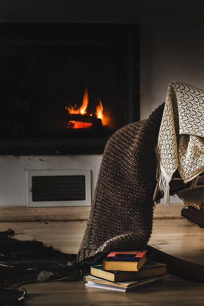 Rocking chair with knit rug, books and cup of tea or coffee before fireplace