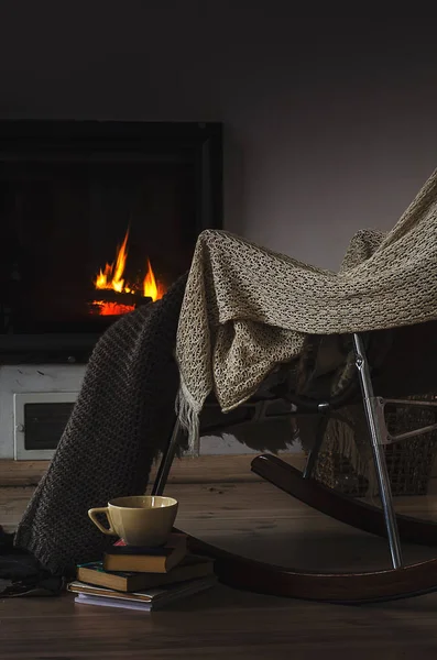 Silla mecedora con alfombra de punto, libros y taza de té o café antes de la chimenea — Foto de Stock