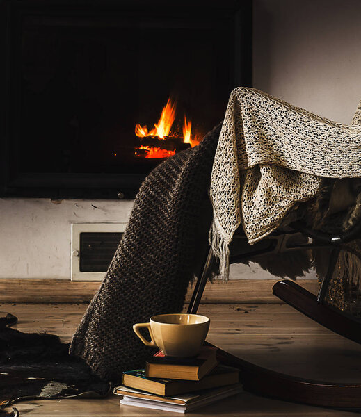 Rocking chair with knit rug, books and cup of tea or coffee before fireplace