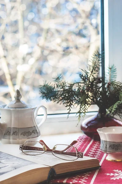 Inverno ainda vida: livro aberto, copos, bule e xícara e árvore de Natal em vaso. Foco seletivo. Decoração de casa, relaxe conceito — Fotografia de Stock