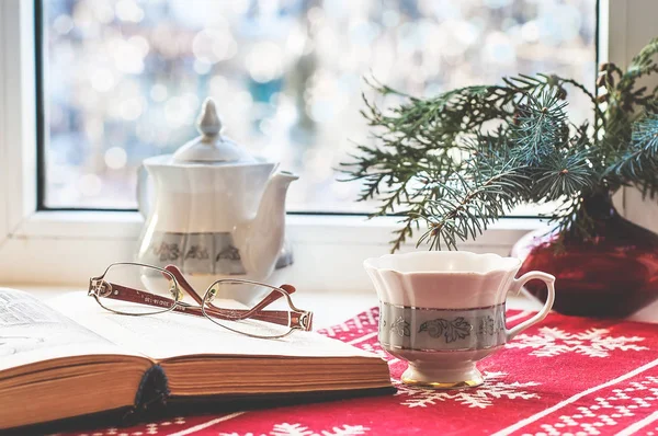 Winter still life : open book, glasses, teapot and cup and christmas tree in vase. Selective focus. Home decor, relax concept