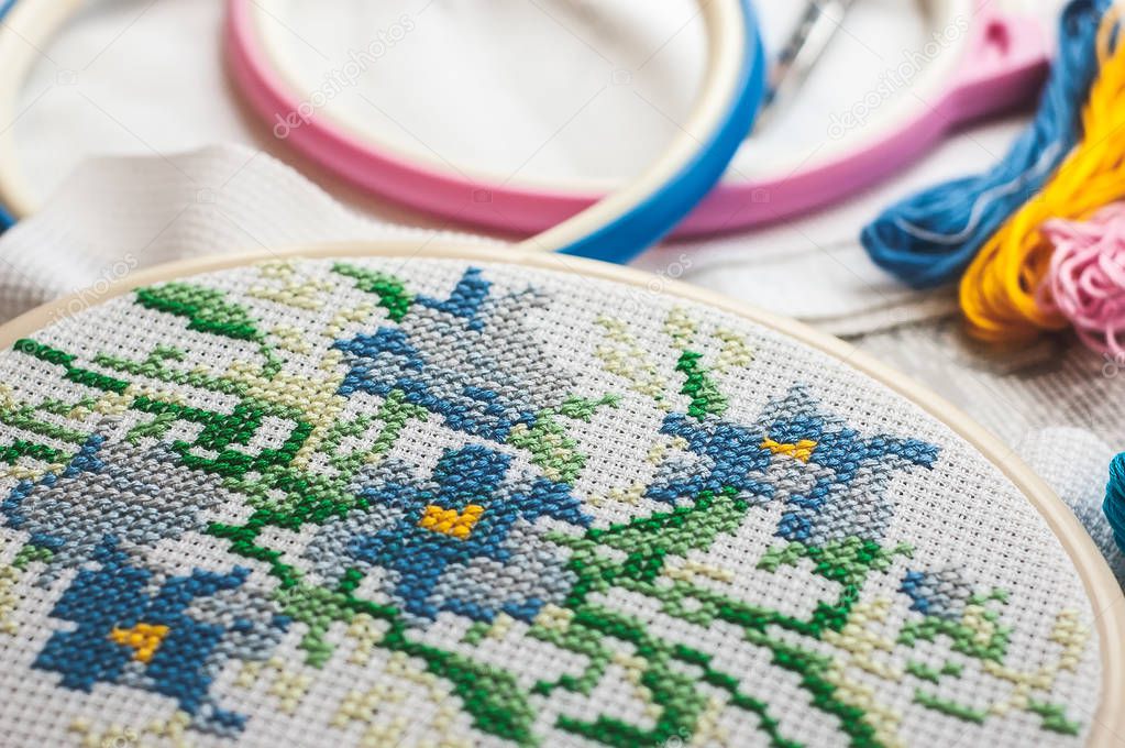 Cross-stitch set : hoop with embroidered pattern, glasses, scheme, scissors, canvas and colorful yarn. Selective focus. Freelance, hobby, handmade home decor concept