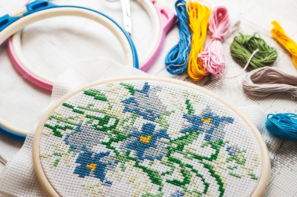 Cross-stitch set : hoop with embroidered pattern, glasses, scheme, scissors, canvas and colorful yarn. Selective focus. Freelance, hobby, handmade home decor concept