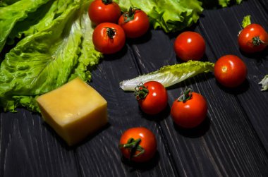 Taze salata malzemeler: domates, küp peyniri ve marul yaprakları siyah ahşap arka plan üzerine. Organik gıda fotoğraf kavramı. Seçici odak