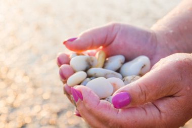 Gün batımında sahilde elinde deniz taşları