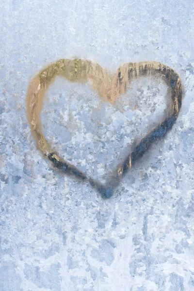 Heart on a frosty winter in the frozen patterns of ice window