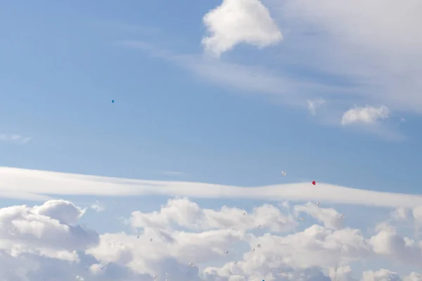 Colorful balloons fly in the blue spring sky with white clouds