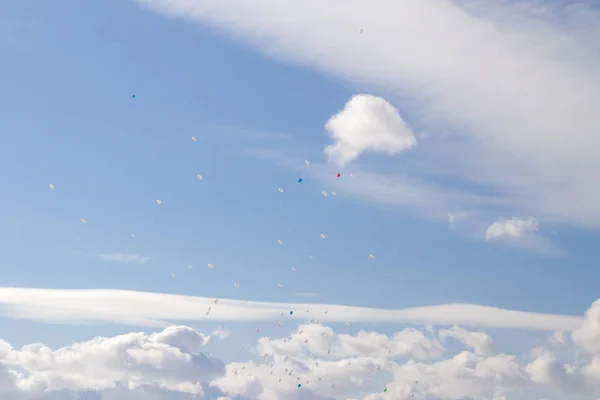 Colorful balloons fly in the blue spring sky with white clouds