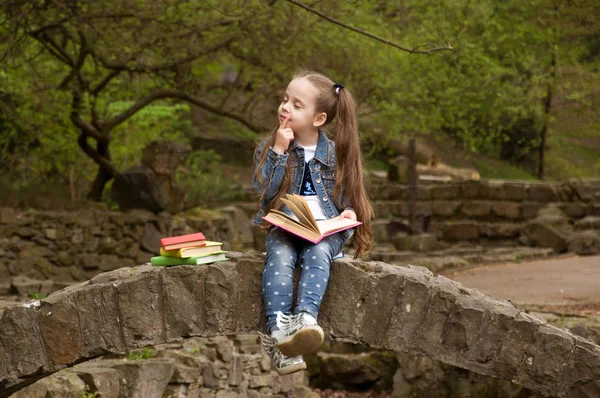 Kis iskolás olvas egy könyvet a természetben. Okos kis pupi — Stock Fotó