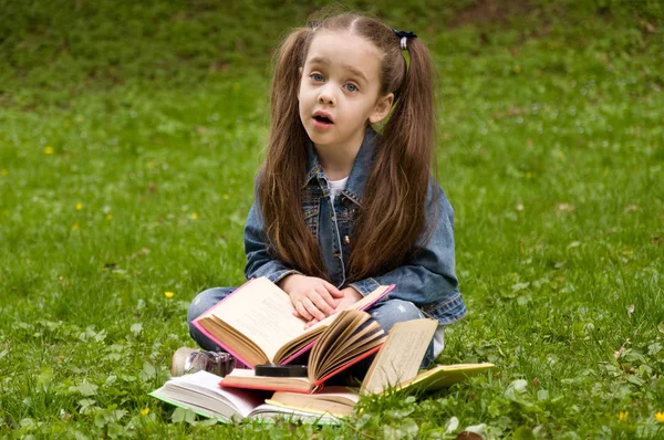 Liten skolflicka läser en bok i naturen. Smart liten pupi — Stockfoto