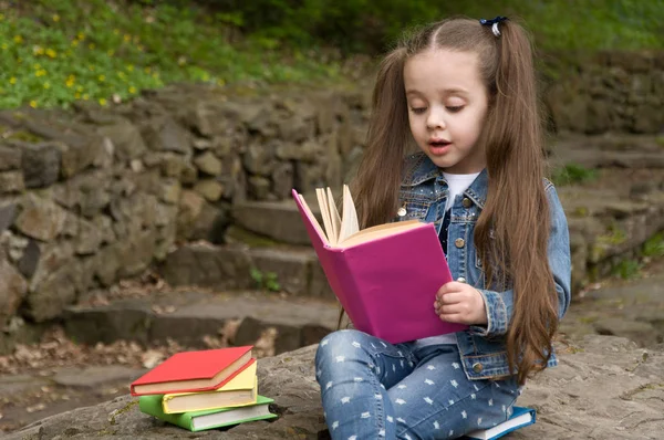 Liten skolflicka läser en bok i naturen. Smart liten pupi — Stockfoto