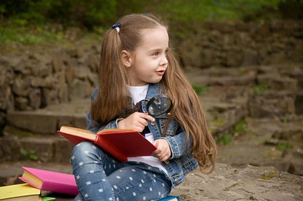 Дівчинка читає книжку зі збільшувальним склом. Розумна маленька р — стокове фото