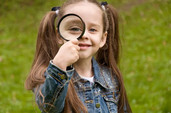 Little girl explores at nature through a magnifying glass — Stock Photo, Image