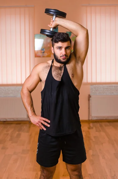 Guapo joven musculoso haciendo ejercicio con mancuernas . — Foto de Stock