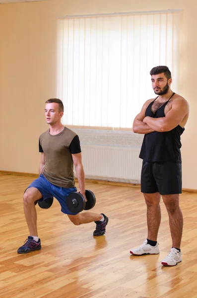 Homem e seu personal trainer exercitando com halteres no ginásio . — Fotografia de Stock