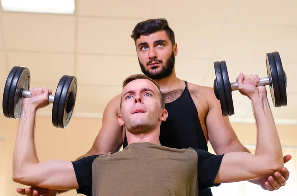 Man and his personal trainer exercising with dumbbells at the Gym. Technique exercises for the shoulders. novice athlete with coach.