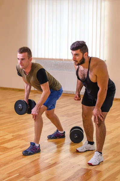 Homem e seu personal trainer exercitando com halteres no ginásio . — Fotografia de Stock