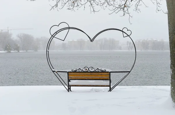 empty snow-covered wrought-iron bench in the form of hearts for couple of lovers in winter park.