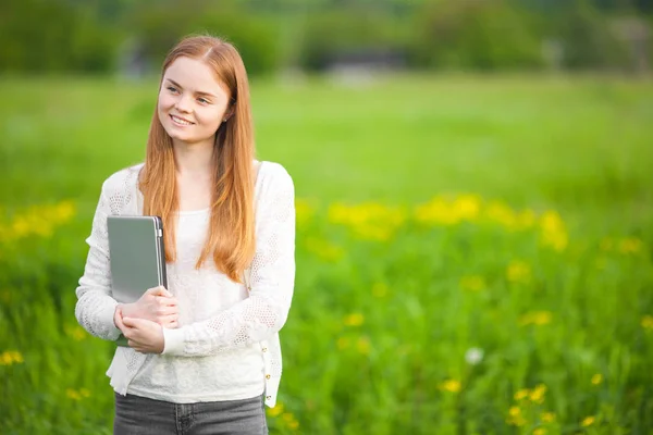 Young freckled meisje landbouwingenieur of bioloog in witte blouse staande in groene veld met notitieboekje en pen tijdens de oogst. — Stockfoto