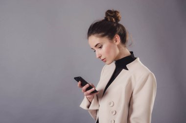 Nötr gri bir arka plan üzerinde izole bir genç çekici kız kullanma smartphone portresi.
