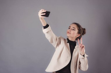 Nötr gri bir arka plan üzerinde izole smartphone ile selfie fotoğraf yapma bir çekici kız portresi.