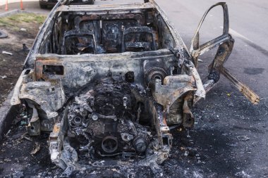 Şehirdeki yolda park etmiş hızlı bir araba yanmış. Araba artığı.